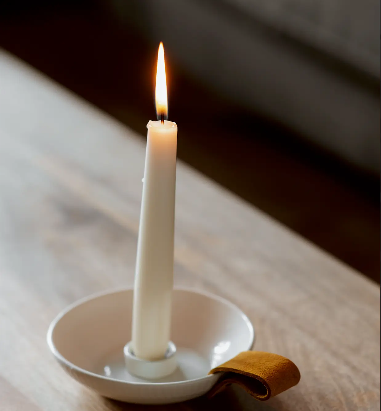 A lit white candle on a wooden table, evoking warmth, reflection, and a calm space for relationship anxiety therapy.