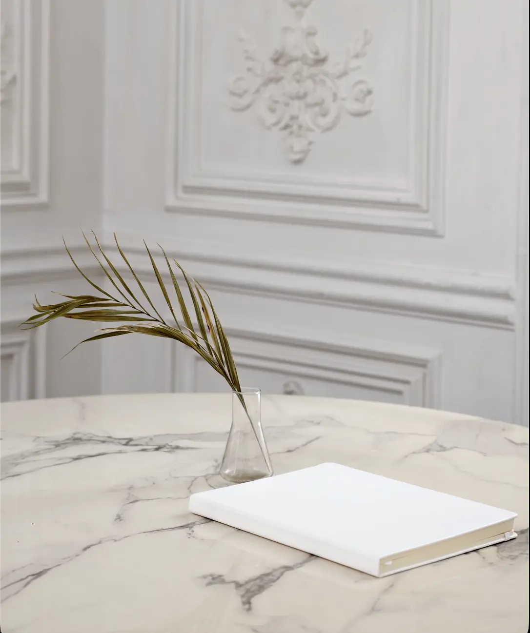 A soft, minimalist image of a white journal and palm leaf on a marble table, used to evoke calm, reflection, emotional clarity after therapy for perfectionism and overthinking.